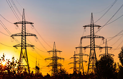 High voltage electric towers at golden sunset. Silhouettes of a number of electricity pylons and trees. Power towers at the background of bright setting sun.