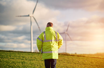 Back view of young male engineer in a wind turbine farm in the b